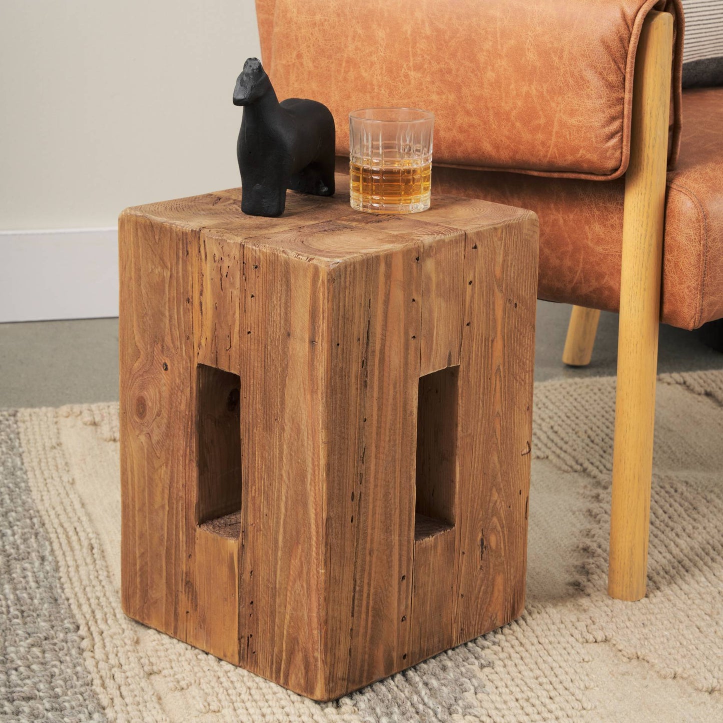 Wooden side table with a glass of whiskey and a black figurine next to a brown leather chair.